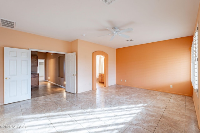 spare room with arched walkways, visible vents, baseboards, and ceiling fan