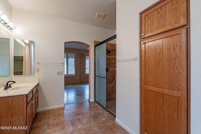 full bathroom with visible vents, tiled shower, baseboards, and vanity