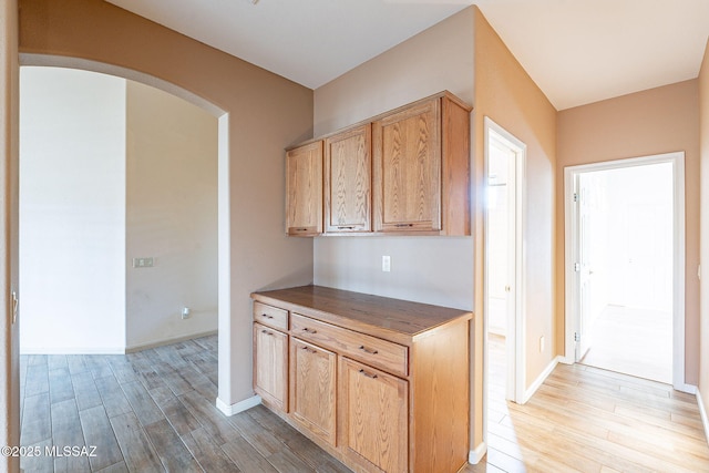 kitchen featuring arched walkways, light wood-style flooring, dark countertops, and baseboards