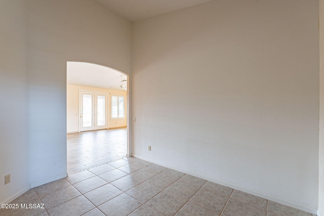 unfurnished room with light tile patterned floors, baseboards, arched walkways, and a high ceiling