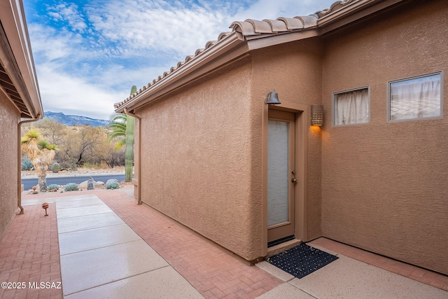 view of exterior entry featuring a tiled roof, stucco siding, a mountain view, and a patio area
