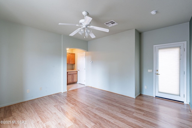 empty room with arched walkways, visible vents, ceiling fan, and light wood-style floors