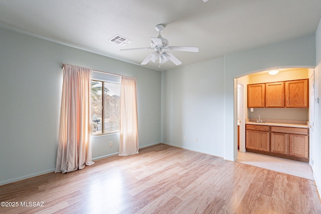 unfurnished living room with light wood-type flooring, visible vents, arched walkways, baseboards, and ceiling fan
