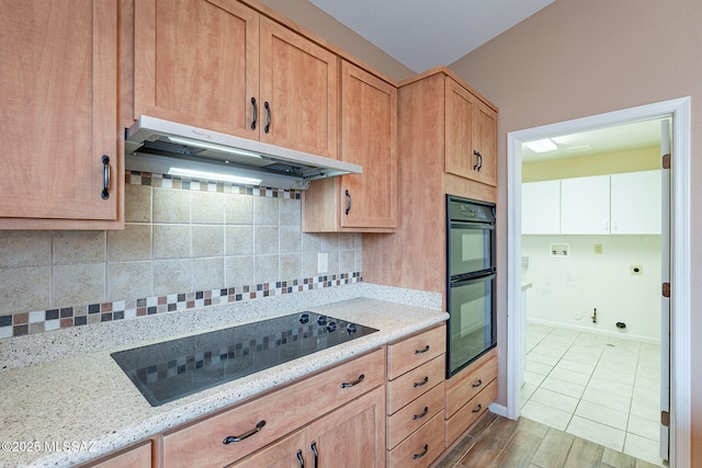 kitchen with black appliances, under cabinet range hood, backsplash, wood finished floors, and light stone countertops