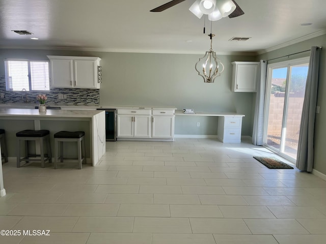 kitchen with decorative backsplash, light countertops, white cabinetry, and ornamental molding