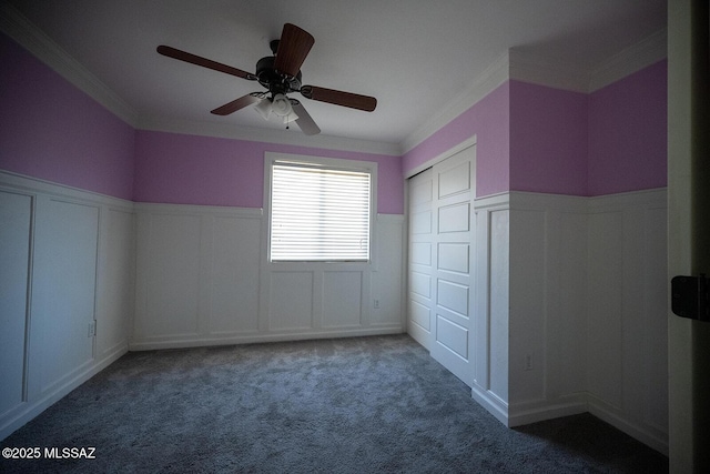 unfurnished bedroom with a wainscoted wall, carpet floors, ceiling fan, ornamental molding, and a closet