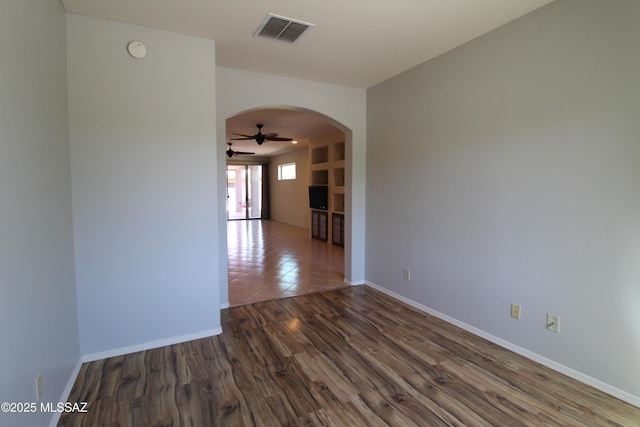 spare room with wood finished floors, ceiling fan, arched walkways, baseboards, and visible vents