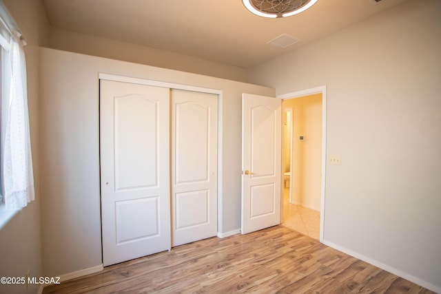 unfurnished bedroom featuring a closet, light wood finished floors, baseboards, and visible vents