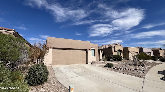 pueblo-style house featuring concrete driveway, a tiled roof, an attached garage, and stucco siding