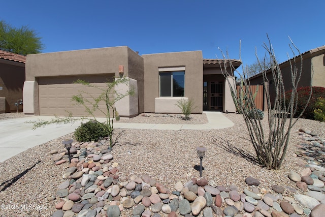 pueblo revival-style home with fence, concrete driveway, an attached garage, a tile roof, and stucco siding