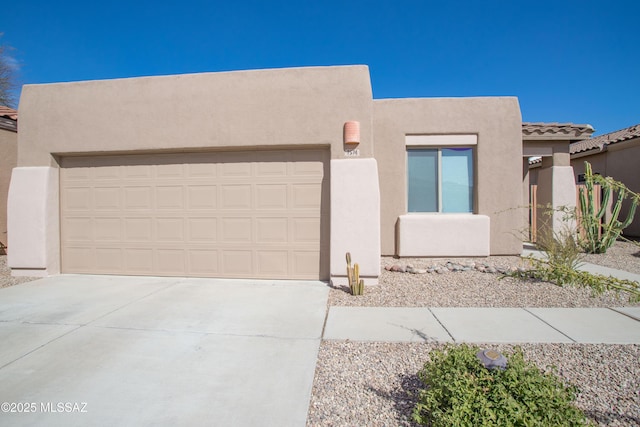 pueblo revival-style home with stucco siding, driveway, a tiled roof, and a garage