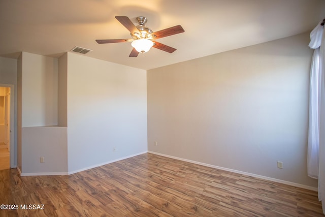 empty room with wood finished floors, baseboards, a ceiling fan, and visible vents