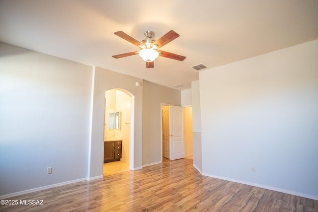unfurnished bedroom with arched walkways, light wood-type flooring, ensuite bathroom, baseboards, and visible vents