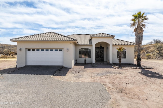 mediterranean / spanish home featuring a garage, driveway, a tile roof, and stucco siding