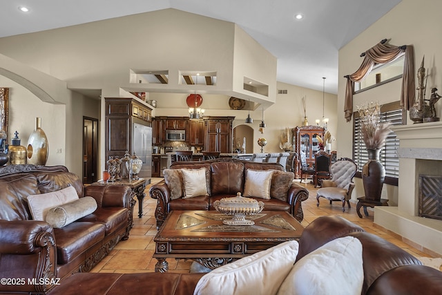 living area featuring arched walkways, high vaulted ceiling, visible vents, a glass covered fireplace, and a chandelier