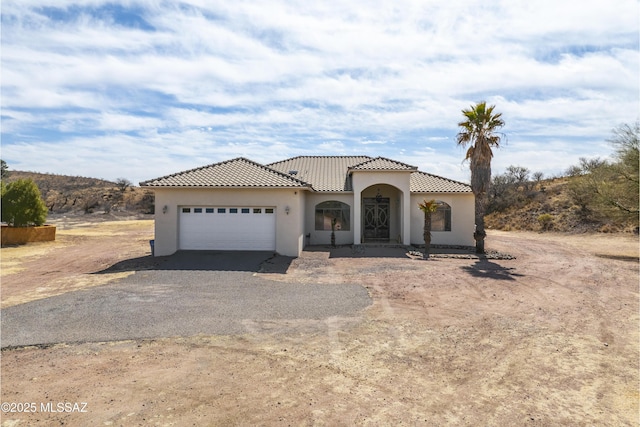 mediterranean / spanish-style house with a garage, driveway, a tiled roof, and stucco siding