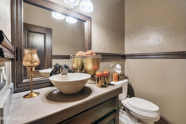 bathroom featuring a textured wall, vanity, and toilet