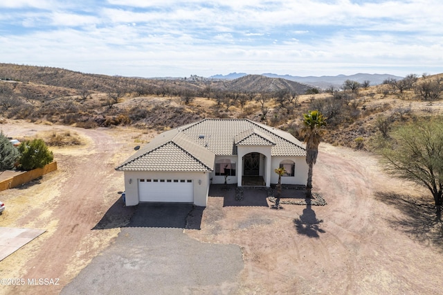 view of front of home featuring driveway, a tiled roof, an attached garage, a mountain view, and stucco siding