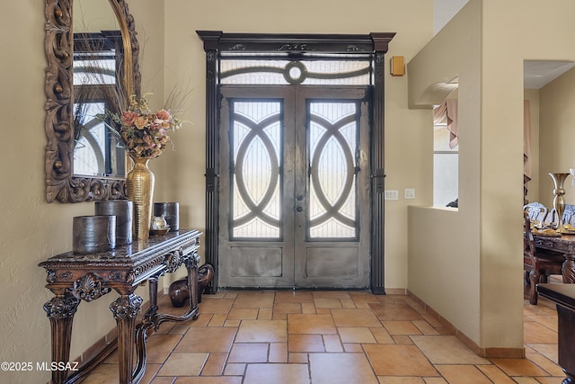 foyer entrance with stone finish floor, baseboards, and french doors