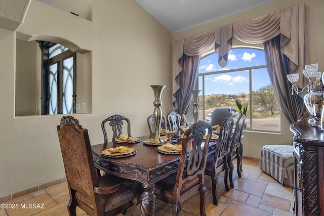 dining space with baseboards, a textured wall, lofted ceiling, and stone tile floors