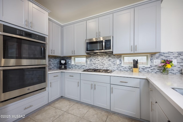 kitchen featuring light tile patterned floors, stainless steel appliances, backsplash, and light countertops