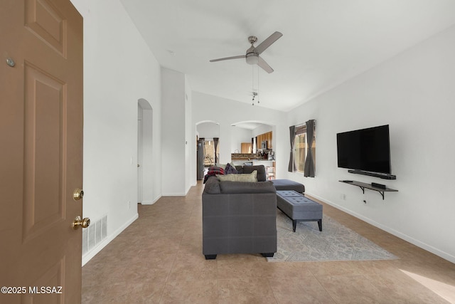 living room featuring arched walkways, light tile patterned floors, a ceiling fan, and baseboards