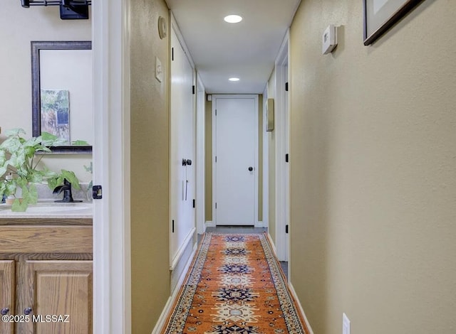 corridor featuring recessed lighting, a sink, and baseboards