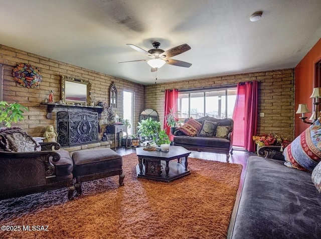 living room featuring a fireplace with raised hearth, brick wall, ceiling fan, and wood finished floors