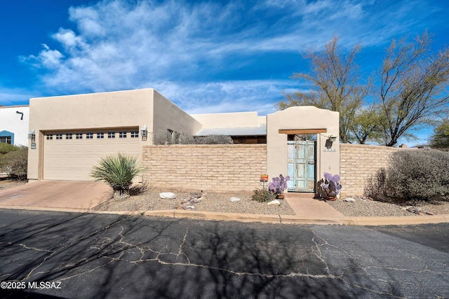 adobe home featuring driveway, an attached garage, fence, and stucco siding