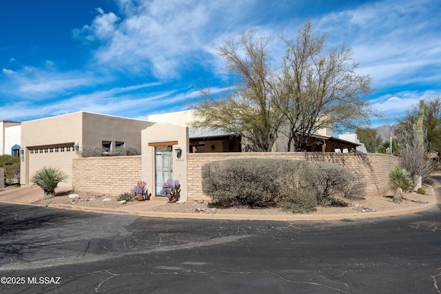 pueblo-style house with a garage, fence, and stucco siding