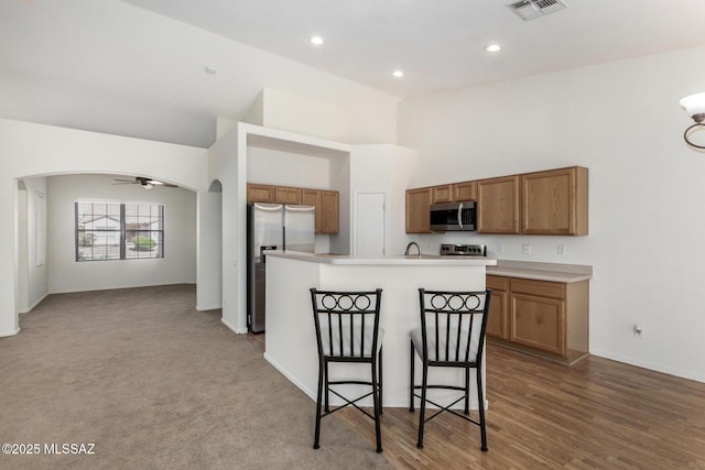 kitchen with arched walkways, a breakfast bar, light countertops, appliances with stainless steel finishes, and an island with sink