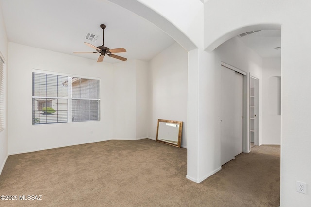 empty room featuring arched walkways, visible vents, ceiling fan, and light carpet