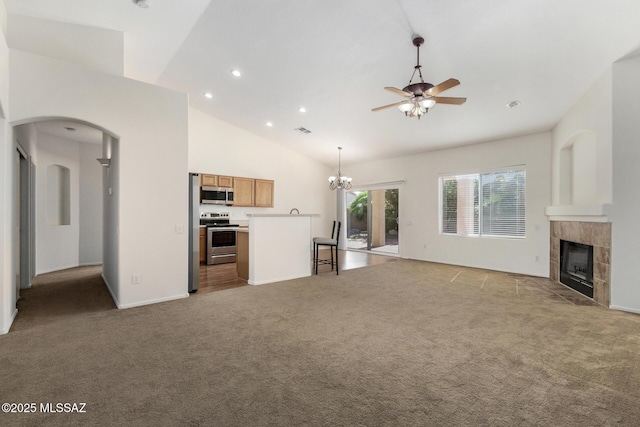 unfurnished living room with arched walkways, high vaulted ceiling, light colored carpet, ceiling fan with notable chandelier, and a tiled fireplace