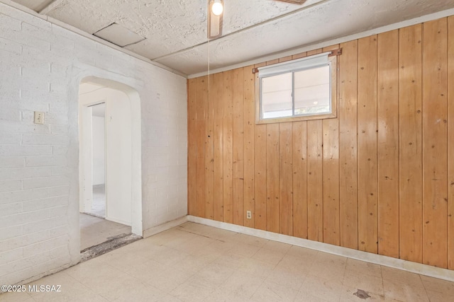 spare room featuring arched walkways, wooden walls, brick wall, and tile patterned floors