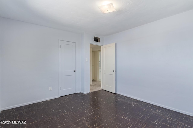 empty room with dark floors, visible vents, and baseboards