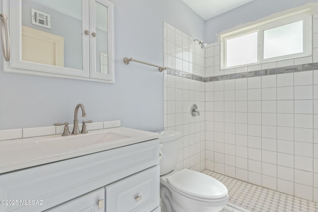 full bathroom with toilet, visible vents, a tile shower, and vanity