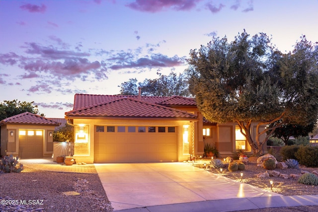 mediterranean / spanish home featuring a garage, a tile roof, concrete driveway, and stucco siding