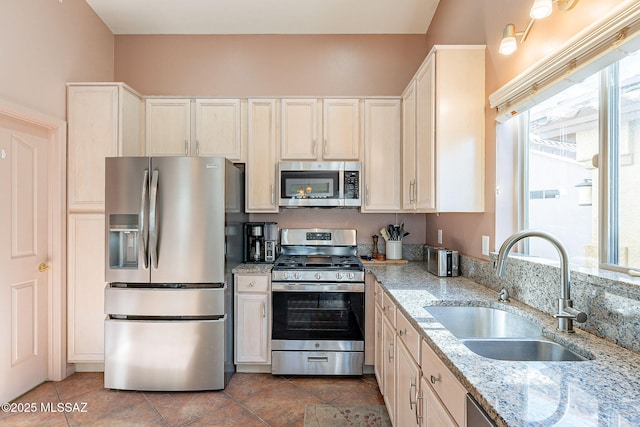 kitchen with appliances with stainless steel finishes, a sink, light stone counters, and light tile patterned floors