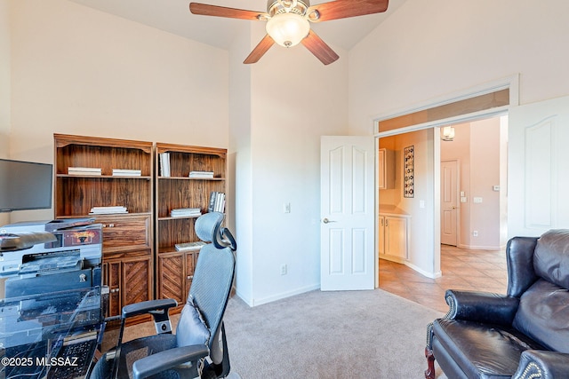 office space featuring light tile patterned floors, light colored carpet, a towering ceiling, a ceiling fan, and baseboards