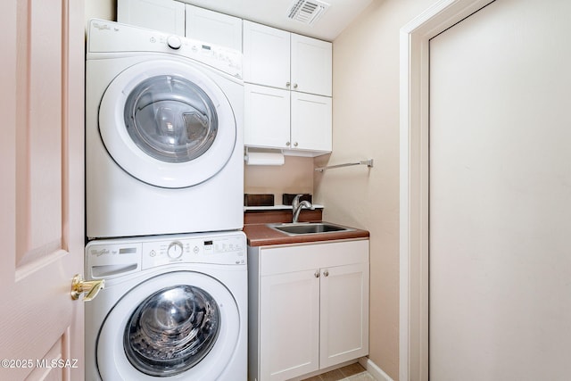 clothes washing area with stacked washer / drying machine, cabinet space, a sink, and visible vents