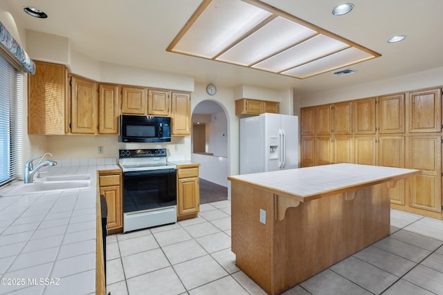 kitchen with white refrigerator with ice dispenser, tile counters, electric range oven, a kitchen island, and black microwave