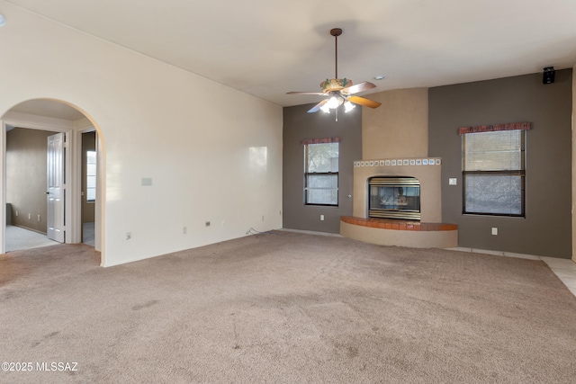 unfurnished living room with arched walkways, lofted ceiling, light carpet, a ceiling fan, and a glass covered fireplace