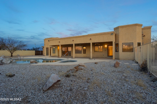 back of house at dusk featuring an outdoor pool, a patio, a fenced backyard, an in ground hot tub, and stucco siding