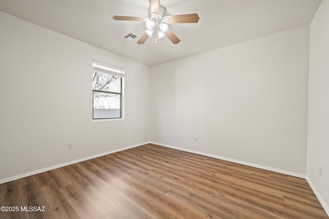 empty room featuring a ceiling fan, visible vents, baseboards, and wood finished floors