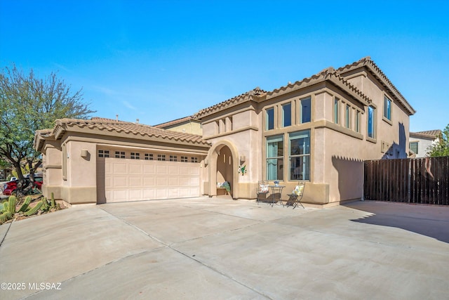 mediterranean / spanish-style house with stucco siding, an attached garage, fence, driveway, and a tiled roof