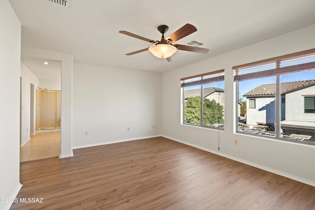 empty room with a ceiling fan, visible vents, baseboards, and wood finished floors