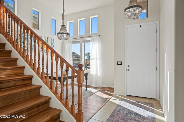 tiled foyer featuring stairway, baseboards, a high ceiling, and a chandelier