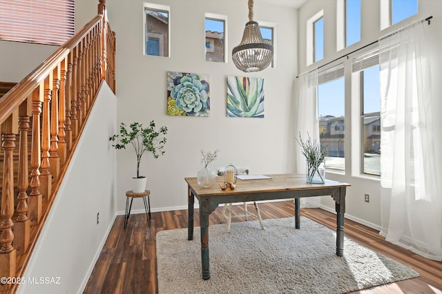 home office with a chandelier, dark wood finished floors, a towering ceiling, and baseboards