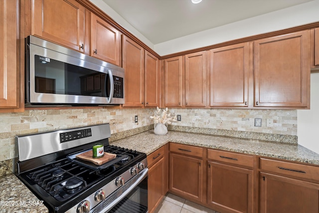 kitchen with light stone counters, brown cabinets, backsplash, appliances with stainless steel finishes, and light tile patterned flooring