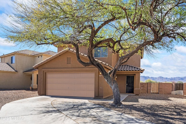 view of front of home with stucco siding, an attached garage, a mountain view, fence, and a tiled roof